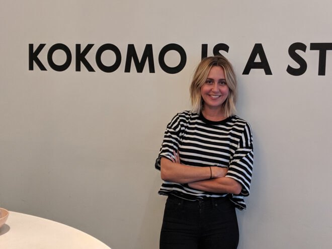Woman in striped shirt smiling and leaning against a wall