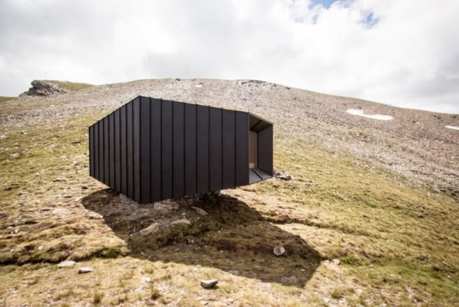 black mountain shelter high in mountains surrounded by greenery