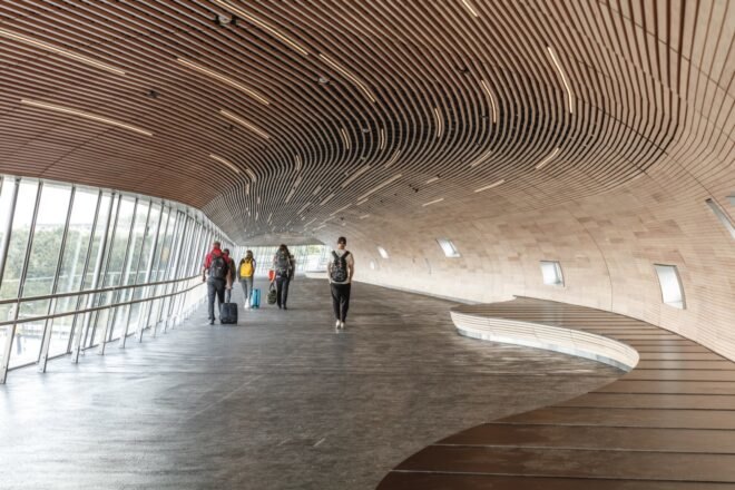 people walking inside tube-like bridge lined in wood