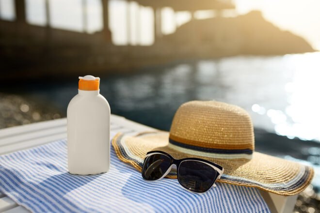 sunscreen, glasses and a hat by water