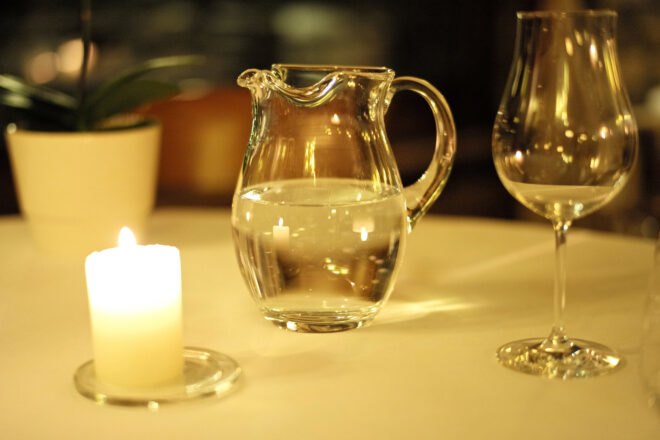 glass pitcher of water on table near a candle