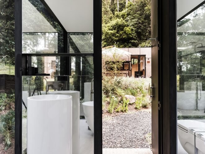 sink against a glass wall and beside a door opening to the forest