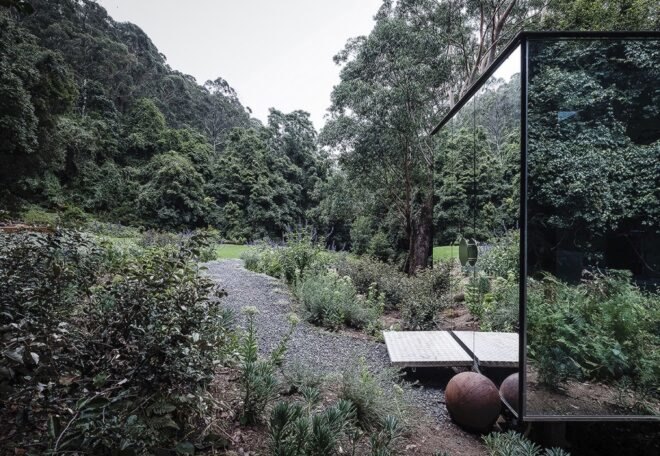 walkway leading to small mirrored building in a forest