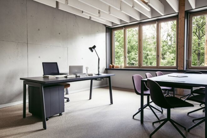 black desks in a room with several windows revealing views of trees