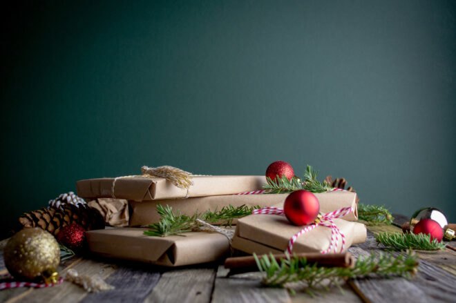 gifts wrapped in brown paper and draped in greenery and red ornaments