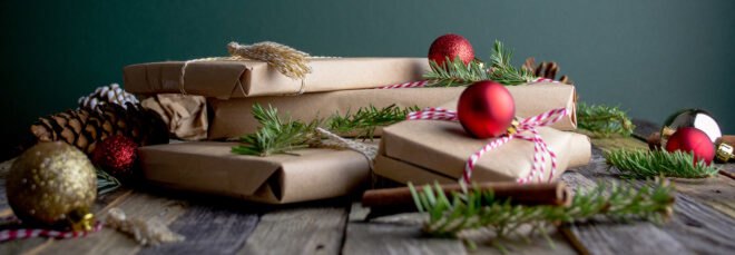 gifts wrapped in brown paper and draped in greenery and red ornaments