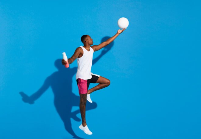 person holding white and coral water bottle with one hand and hitting a ball with another hand