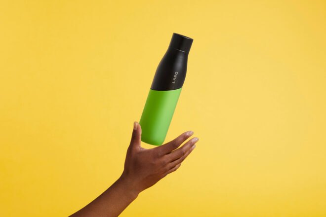hand tossing black and green water bottle in the air