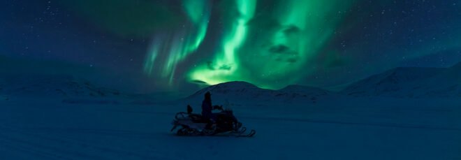 Person on electric snowmobile looking at northern lights