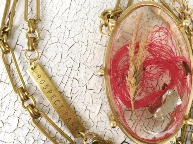 pink string, foil wrapper and two dead plants inside a large gold pendant necklace