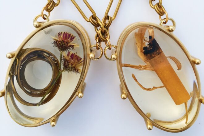 two gold pendants, one filled with dead flowers and one filled with a cigarette butt
