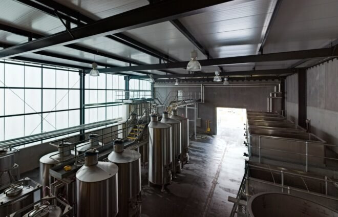 a view of the wine barrel room from from the observation area, showing an open exit area on the opposite wall where light is coming in