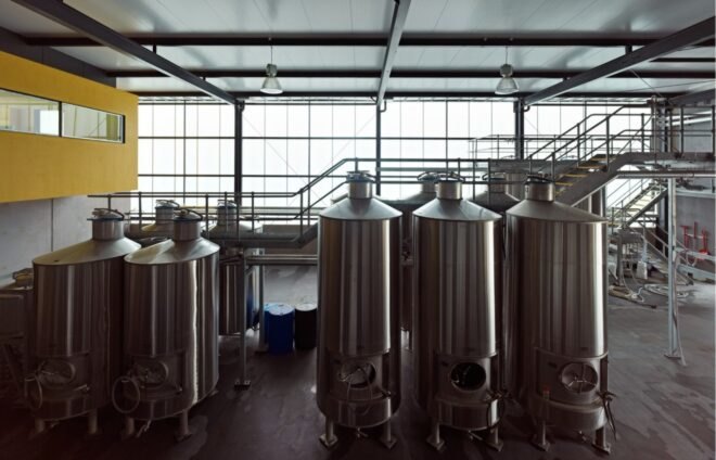 interior of the winery showing five silver wine barrels in the foreground and more in the background. a yellow overlook area in the top left.