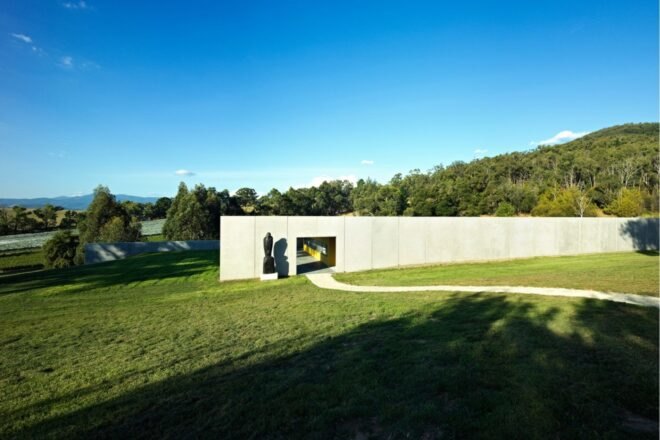 a side angle of a long gray cement structure with an open walk-through area. trees in the background