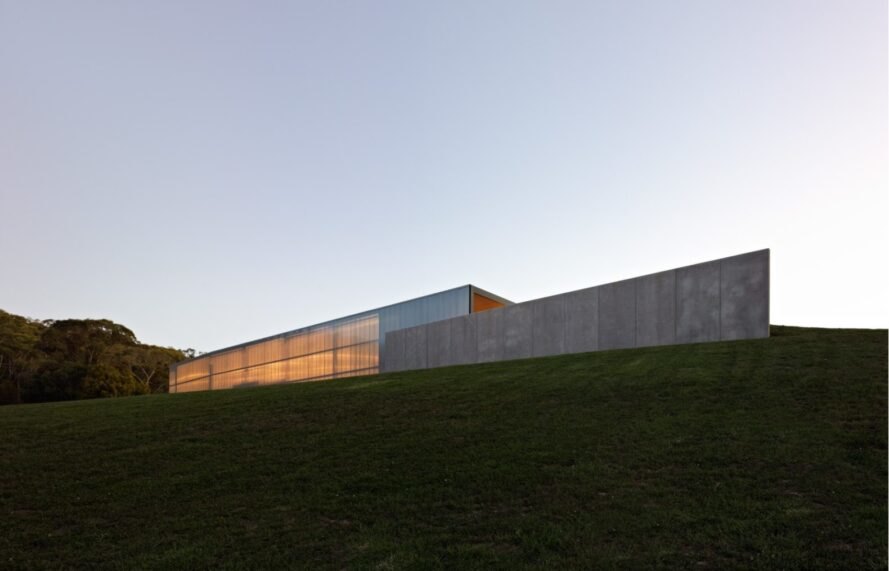 lights illuminate the outer wall of one of the gray buildings (left). the buildings are atop a hill of green grass