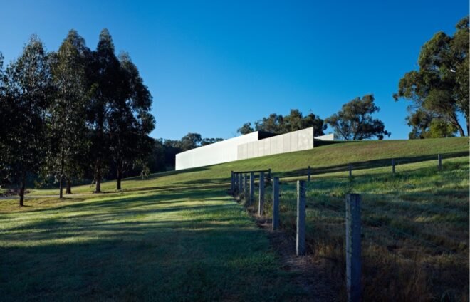 two gray buildings, with one slightly in front of the other, creating a tiered look. the buildings are atop a hill of green grass