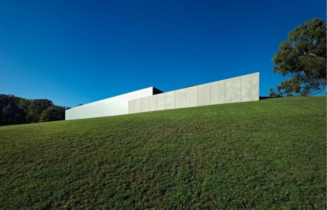 two gray buildings, with one slightly in front of the other, creating a tiered look. the buildings are atop a hill of green grass