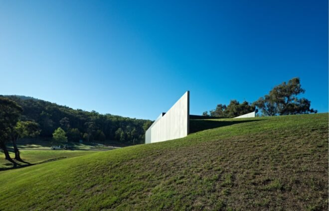 a large cement structure on top of a green hill with trees in the background and a blue sky above