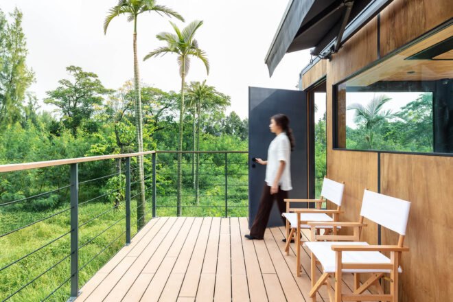 a woman walks out a dark colored door out onto a balcony with a wood floor.