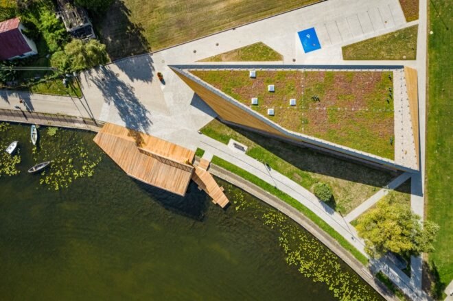 aerial view of green-roofed, triangular wood building near water