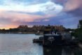 a lake with the Bota Bota structure floating on it and building in the background with a pink, purple and blue sky overhead