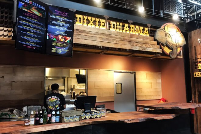 A restaurant counter with yellow lighting and the Dixie Dharma sign hanging above it, with an elephant logo to the right