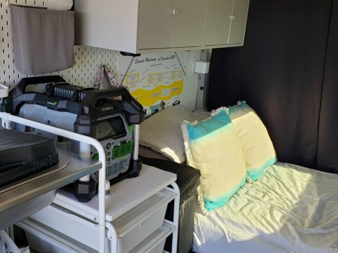 interior space of converted van, focusing on the head of the bed and a set of drawers with a power station stacked on top