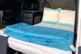 interior space of converted van, focusing on the bed, which has a blue comforter and blue gradient pillows