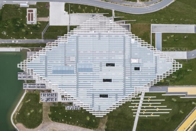 aerial view of glass building with white rhomboid roof covered in skylights