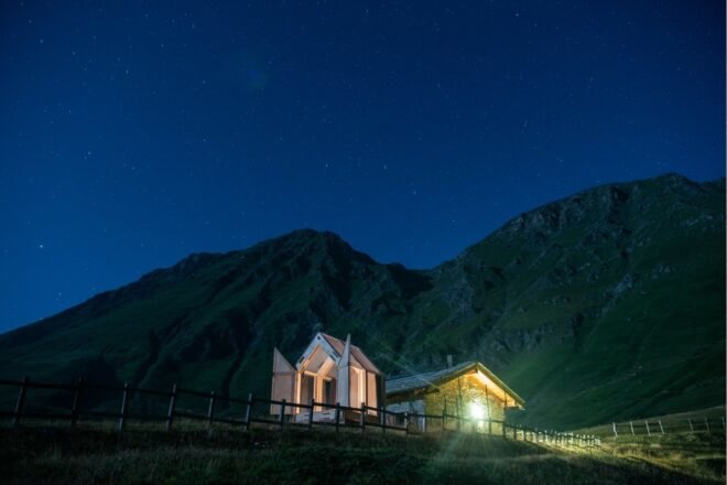 small cabin with transparent walls lit from within at night