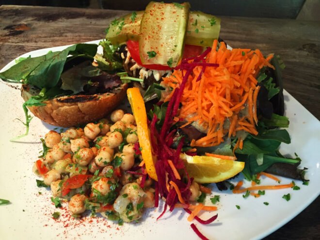 a plate of food featuring garbanzo beans, sliced cucumber, shredded carrots and lemon slices