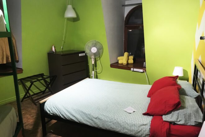 a small bedroom with bright green walls, a window, a dresser in the corner of the room and a bed with two red pillows