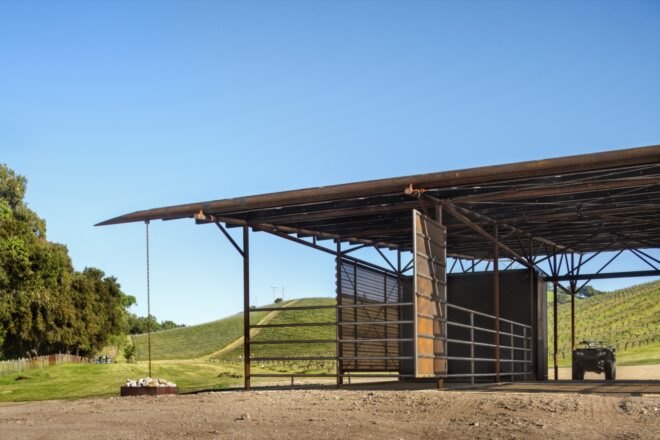 a side view of a barn with a vehicle inside the barn. in the background are rolling green hills with trees to the left.