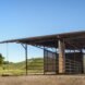 a side view of a barn with a vehicle inside the barn. in the background are rolling green hills with trees to the left.