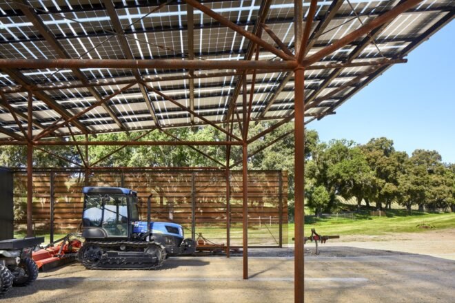interior of a barn with a blue tractor inside it. to the right are green trees.