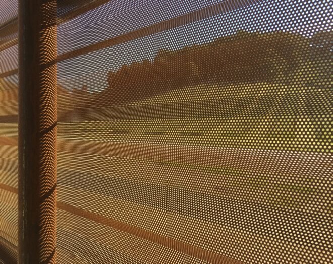 the walls inside the barn, with a wooden post separating two panels with a pattern of tiny pinholes poke through them.