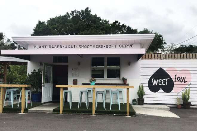 Exterior of a building with two hearts making the Sweet Soul restaurant sign and a wood bench with stools right outside the front door of the restaurant
