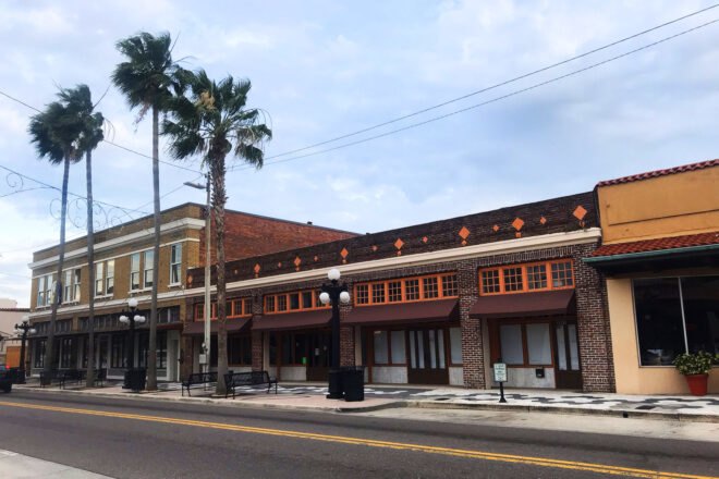 A street in front of a row of downtown buildings with palm trees lining the sidewalk