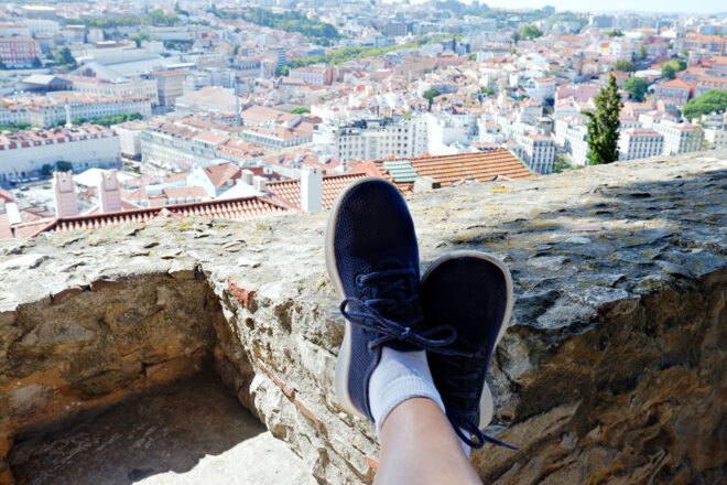 feet in blue sneakers propped up on rock with city views below