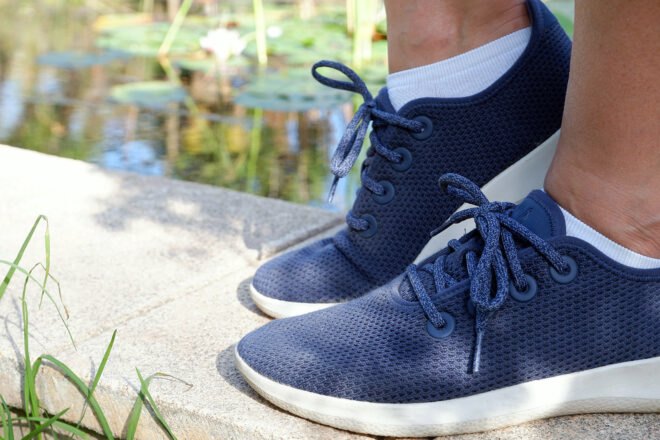 feet in blue sneakers standing on a ledge near a pond