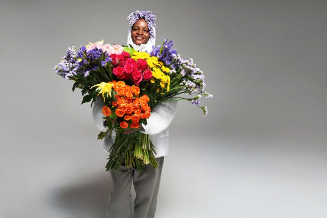 person in puffer jacket holding massive, multicolored bouquet of flowers