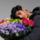 Person wearing puffer coat and smelling multicolored flower bouquet