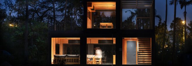 a nighttime shot of the exterior of a building consisting of five cube-like blocks with glass walls framed in dark wood