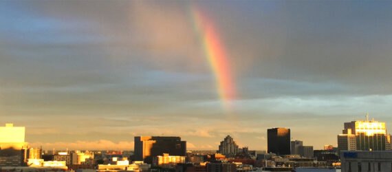 a shot of the horizon with city buildings in the foreground and a rainbow in the sky overhead