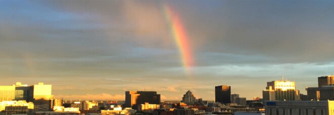 a shot of the horizon with city buildings in the foreground and a rainbow in the sky overhead