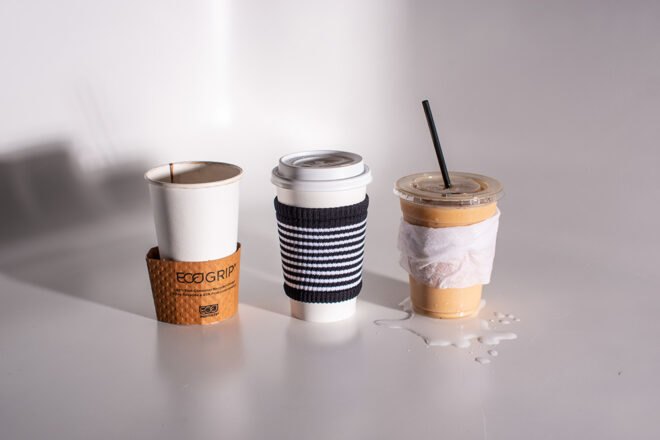 one coffee cup wrapped in cardboard sleeve, one cup wrapped in a napkin, and one cup wrapped in cloth coffee sleeve