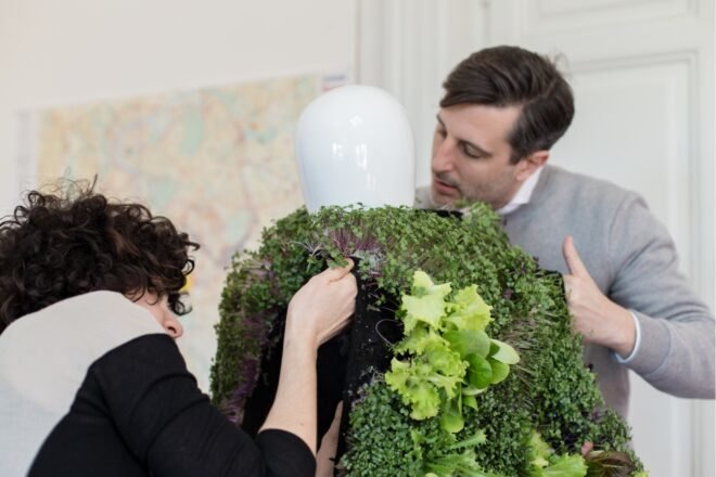 two people outfitting a mannequin with a garden vest