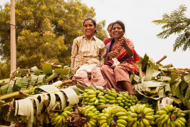 two women sit on top of a pile of bananas and banana leaves