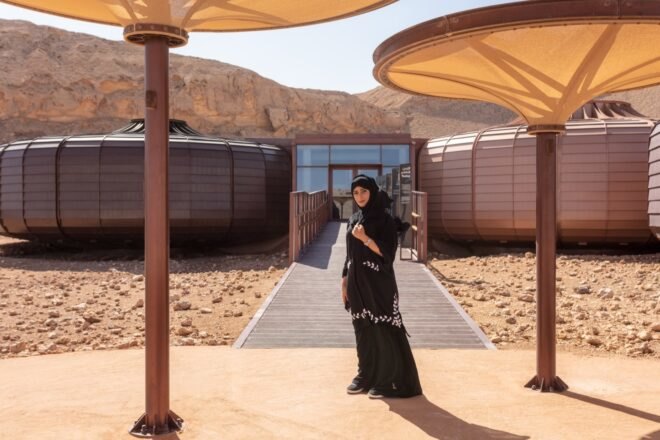 a person in what appears to be a black chador, standing in front of a building with two circular structures