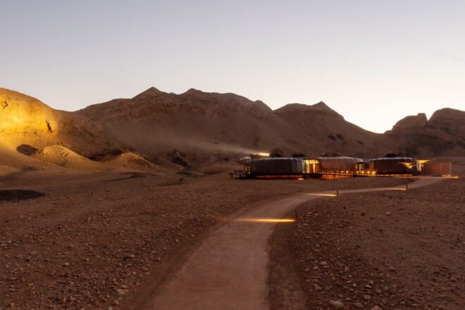 a night view of a driving path through the desert to a lit up building